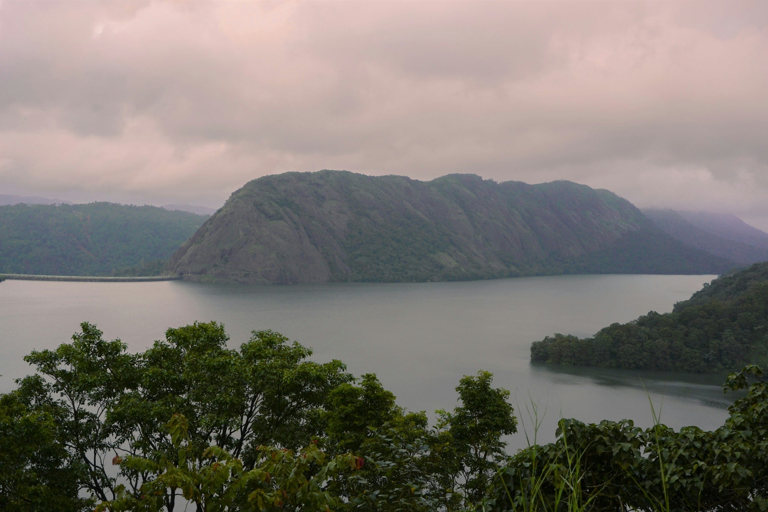 A misty reservoir beneath a forested hill